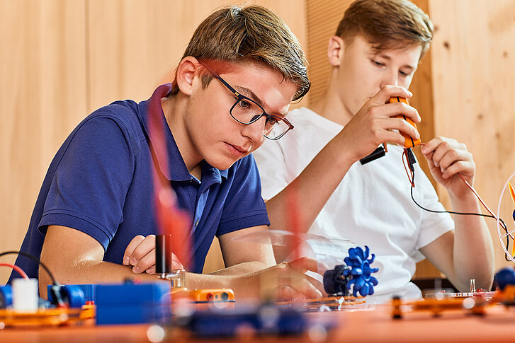 Zwei Jungen basteln mit Elektronik-Bauteilen. Einer der Jungen verbindet gerade zwei Teile miteinander.